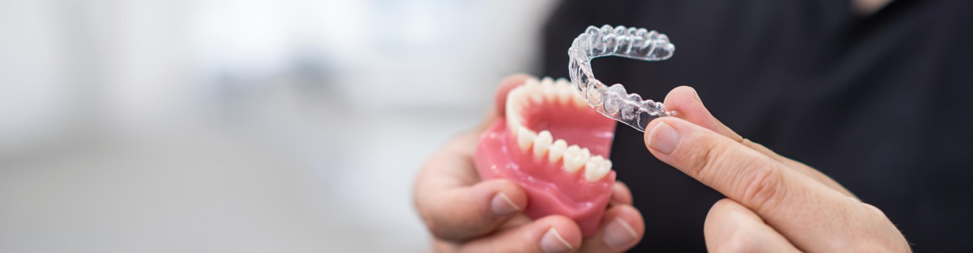 Close-up of a clear orthodontic aligner being held above a dental model of teeth, demonstrating clear aligner treatment.